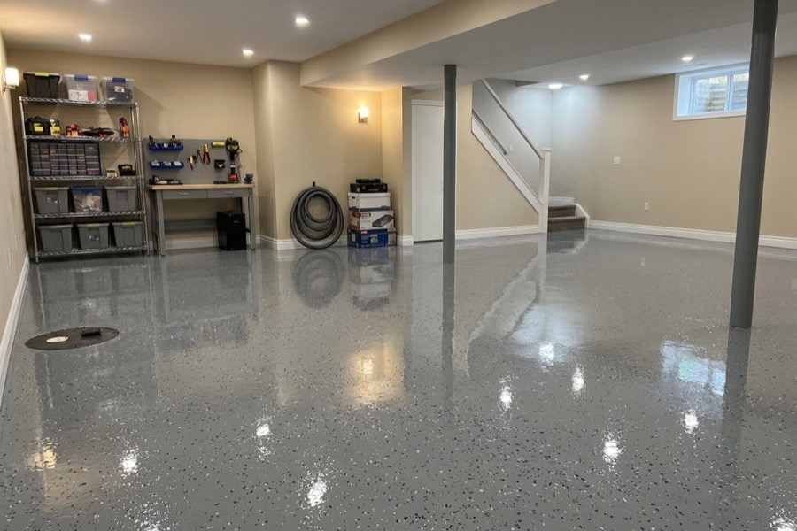 A finished basement with a light grey flake floor and a gloss topcoat, running past the support posts to the stairs.